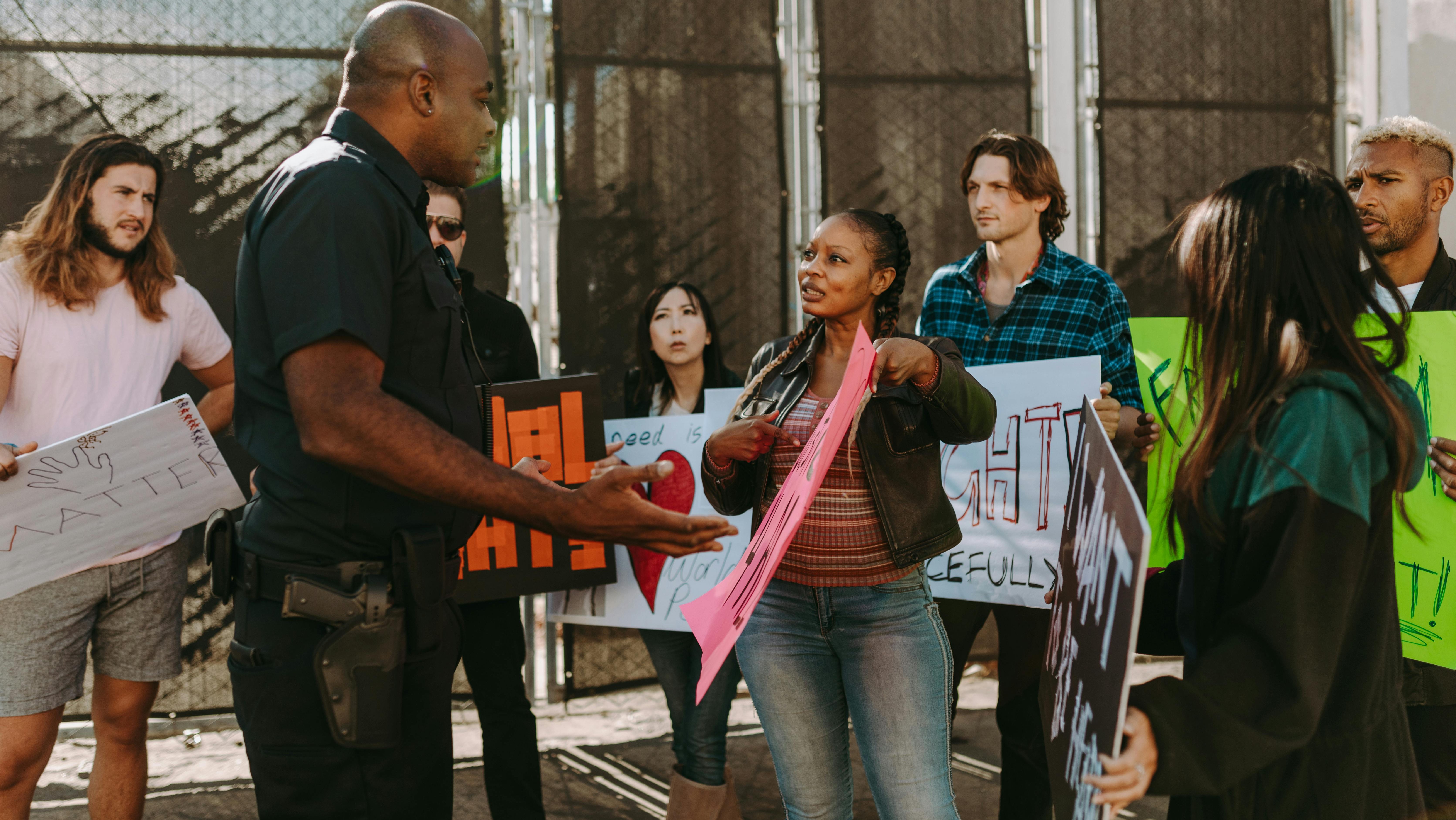 Група протестувальників із плакатами обговорює свої вимоги з поліцейським під час демонстрації