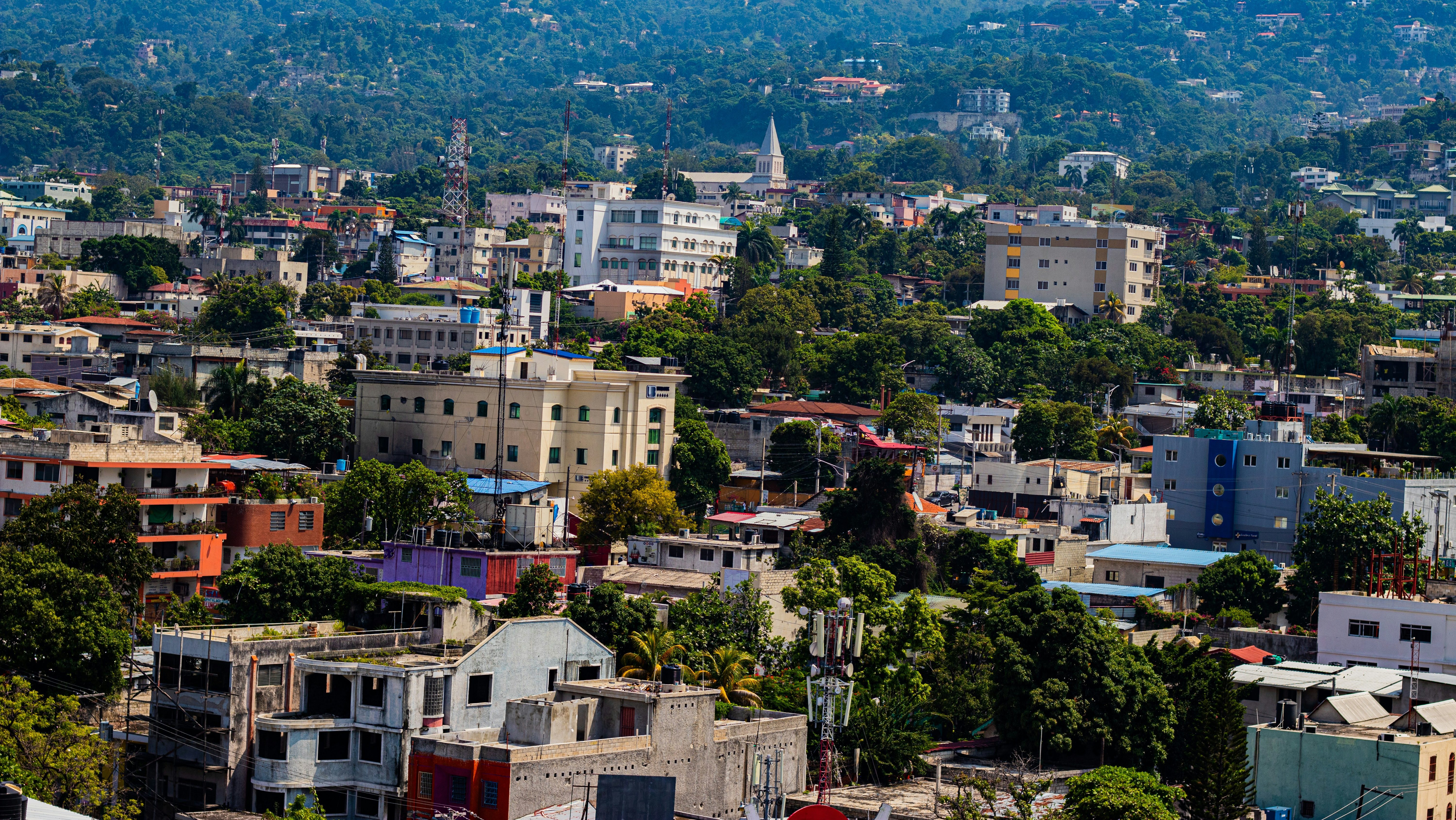Панорамний вид на місто в Гаїті з яскравими будівлями, зеленими деревами та гірським ландшафтом на задньому плані